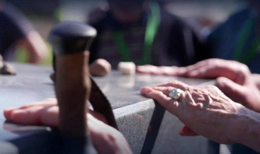 Survivors touch the memorial stone marking the 80th anniversary of their liberation